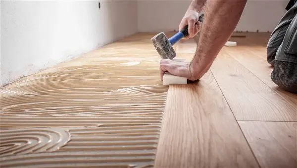 Un ouvrier pose du parquet au sol d'une pièce
