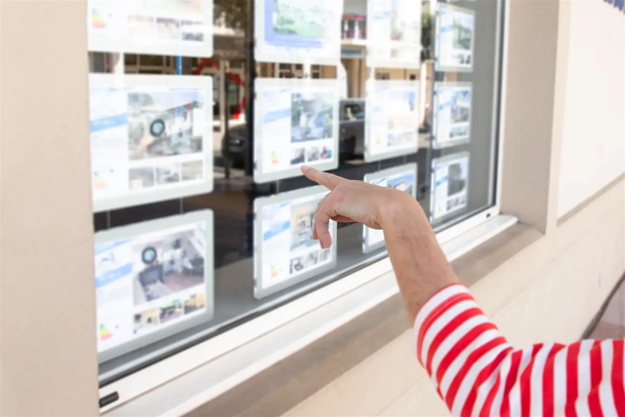 Une personne devant une agence immobilière pointe du doigt une annonce.