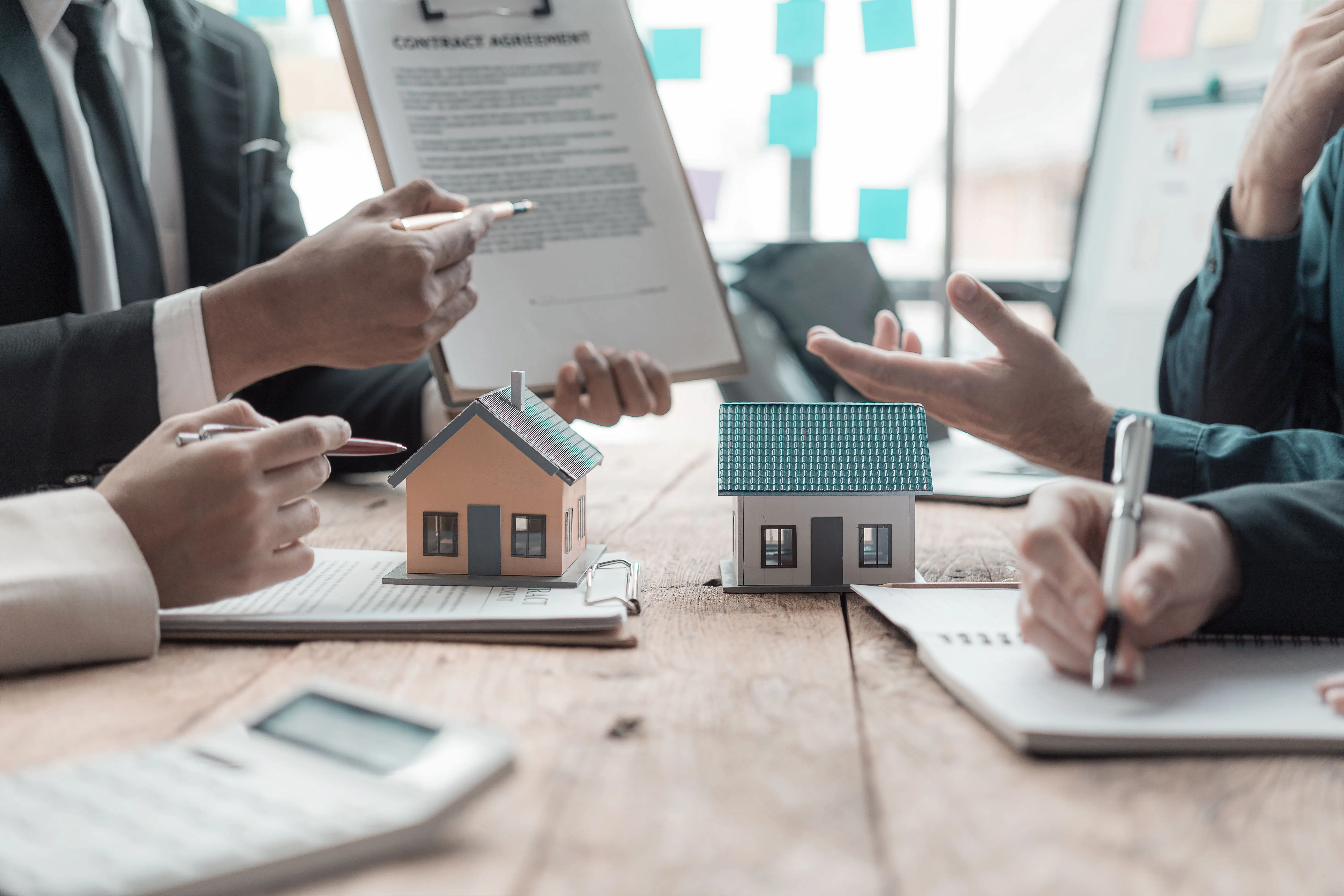 deux petites maisons posées sur une table de réunion et des gens discutent.