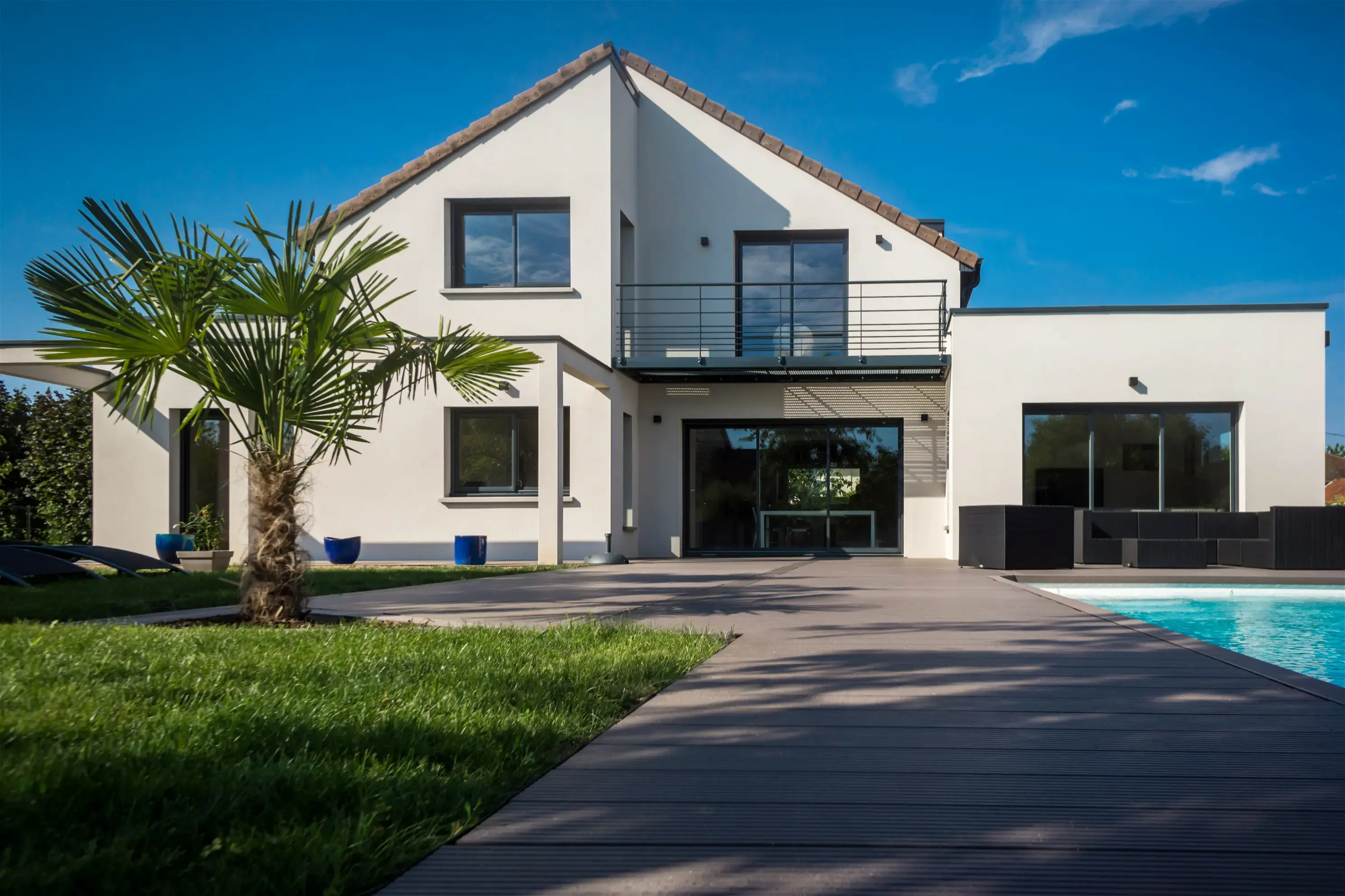 Façade d'une maison avec un jardin, un palmier et une piscine, sous un ciel bleu